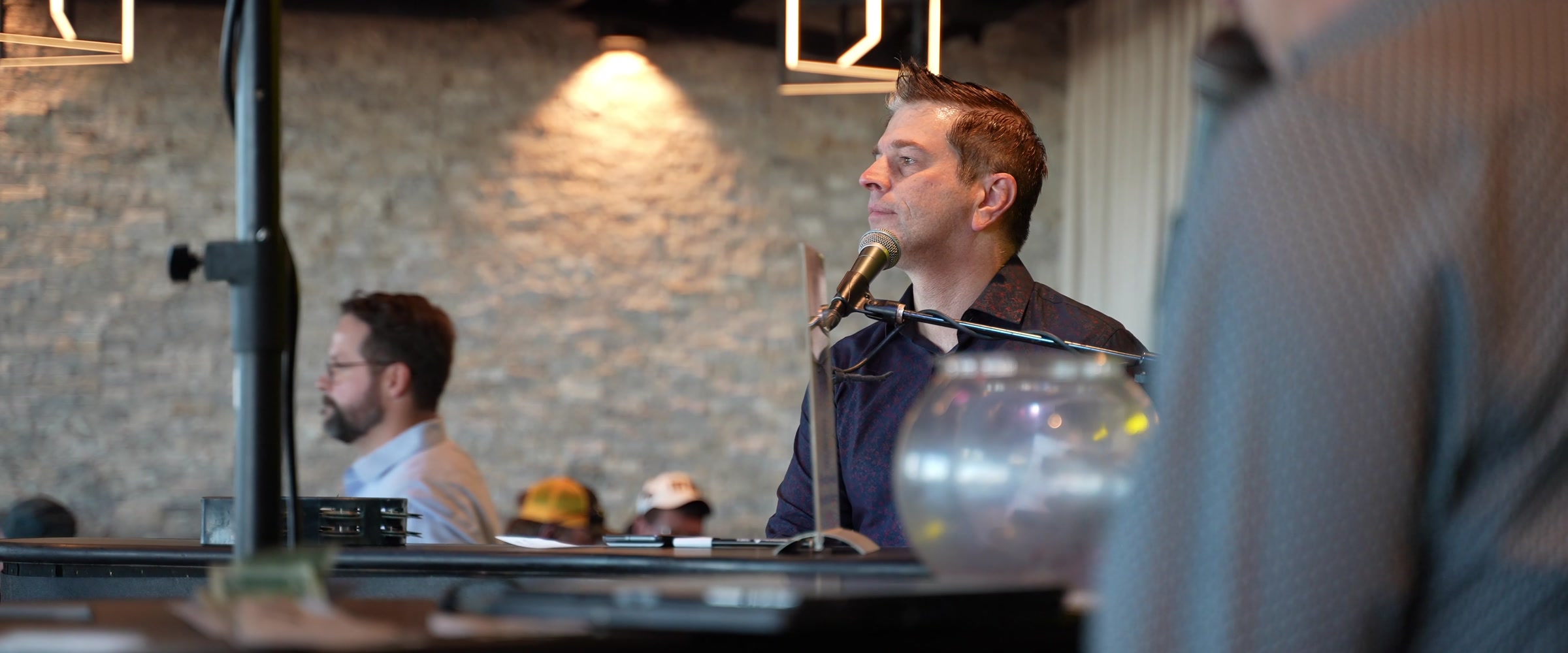 Adam Nelson seated at a piano microphone during a Midwest Dueling Pianos performance.