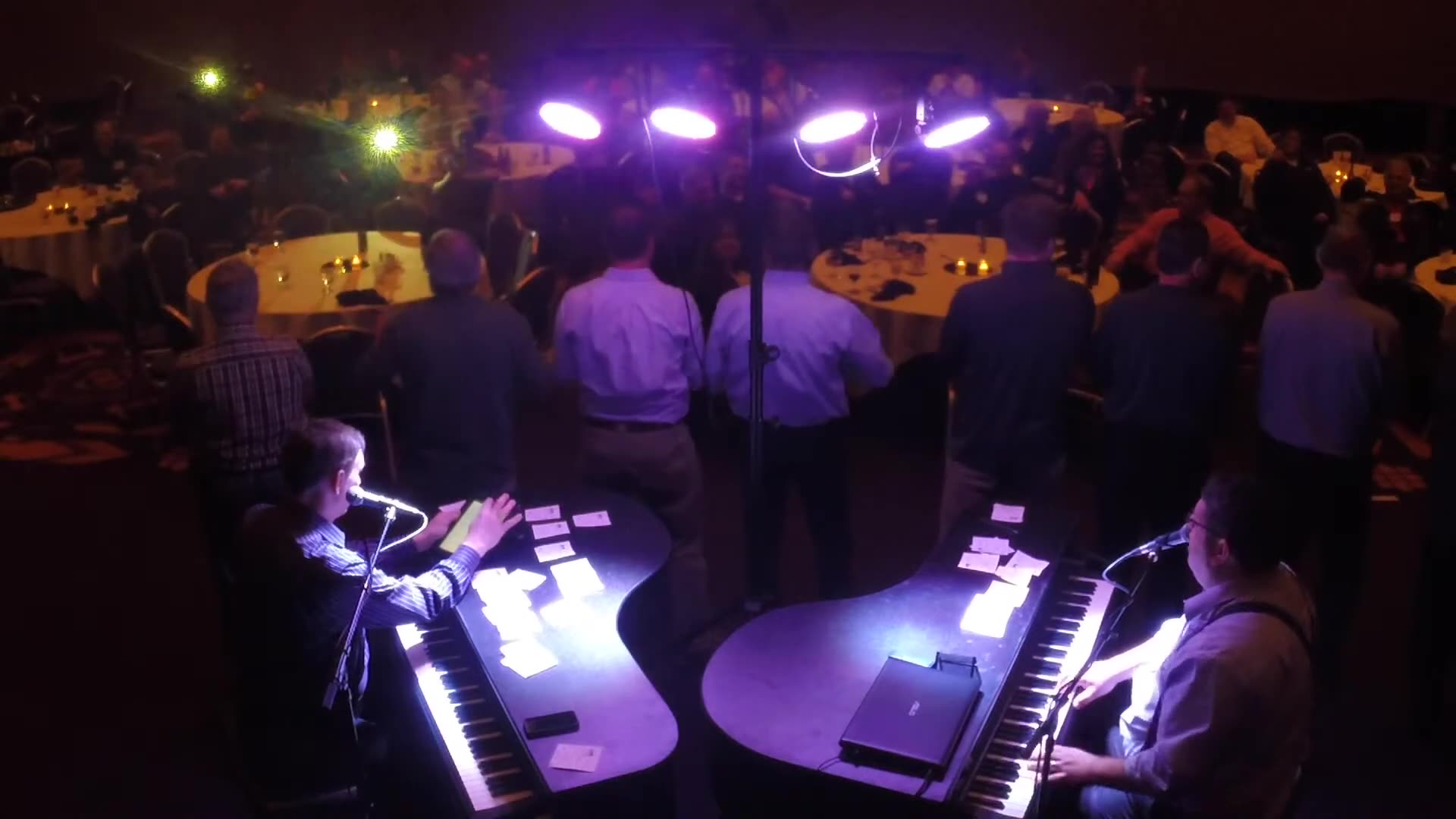 Guests gathered around two pianists during a Midwest Dueling Pianos performance.